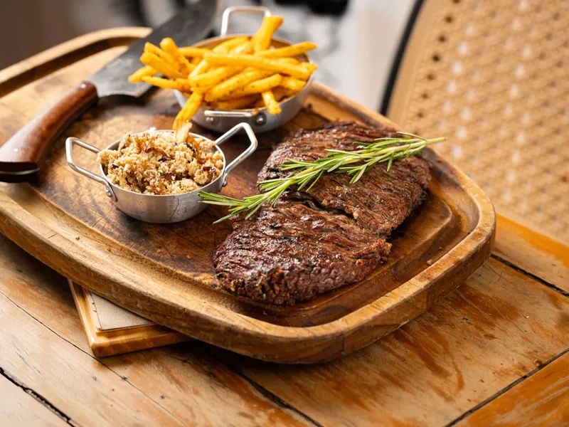 Corte de carne na tábua de madeira, com fritas e farofa