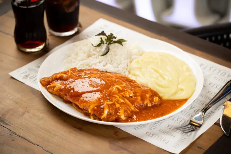 Prato servido no almoço do Família Paulista: filé à parmegiana com arroz branco e purê, sobre papel de mesa da casa.