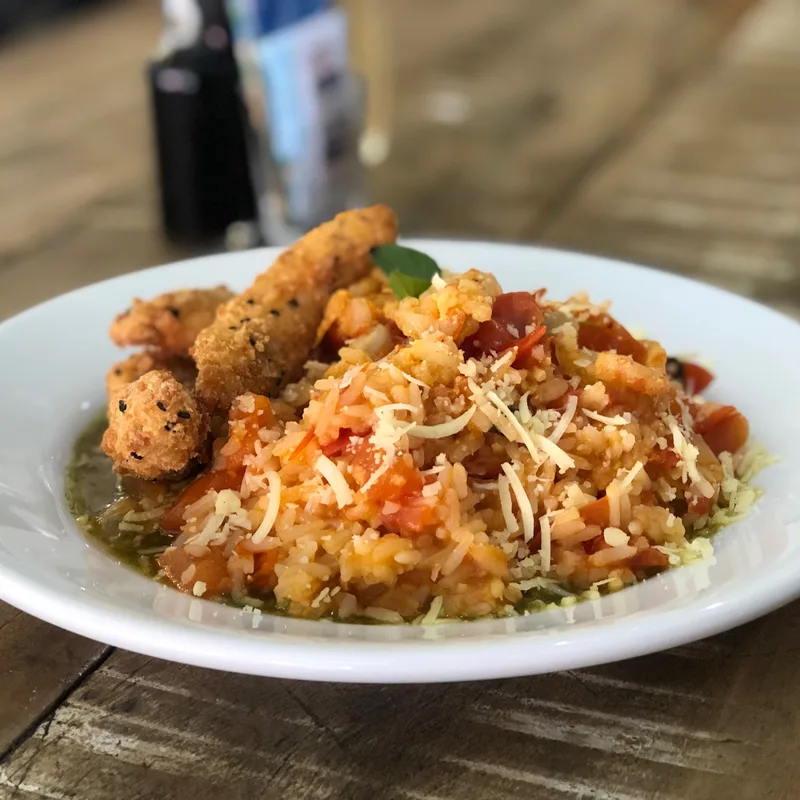 Prato do dia servido no almoço do Família Paulista: arroz cremoso com tomate e queijo ralado, com iscas empanadas polvilhadas de gergelim preto e uma folha de manjericão.